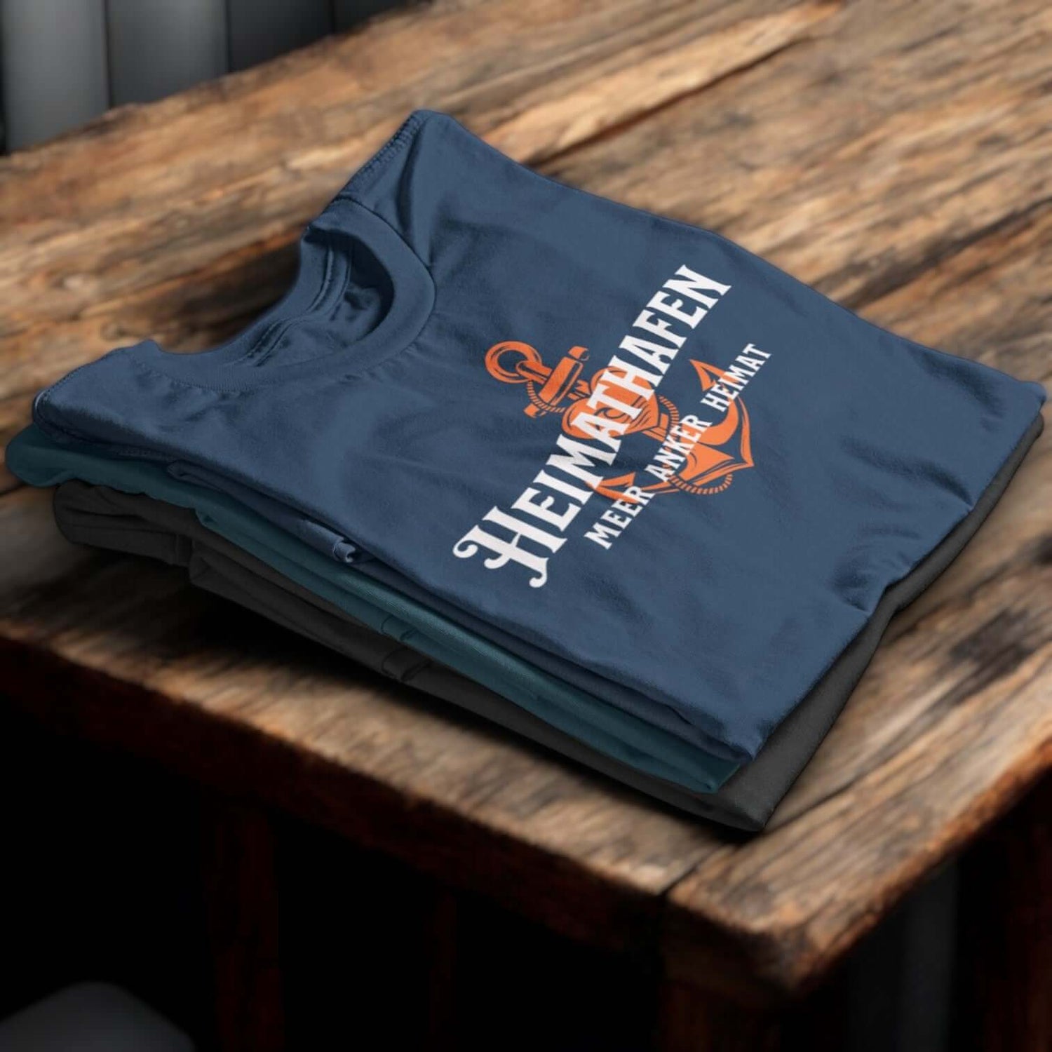 Stapel maritimer Herren-T-Shirts, oberstes Shirt mit Anker aufdruck und Schriftzug Heimathafen – maritime Kleidung für Herren